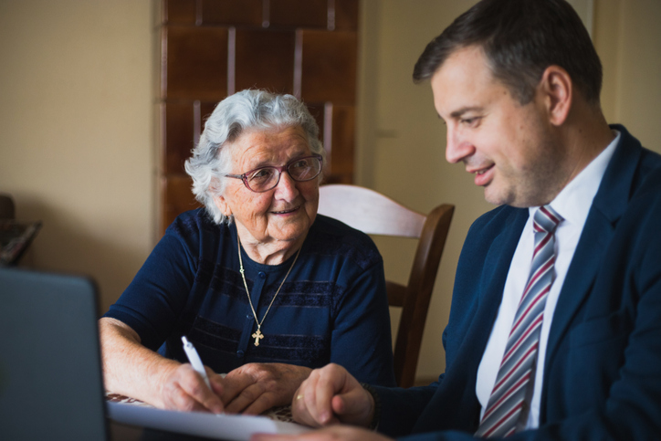 Senior woman signing document at home in the presence of a lawyer.